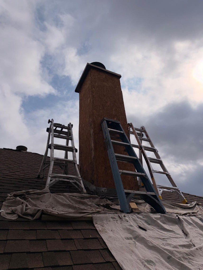 OSB chimney chase on a roof with ladders and drop cloths