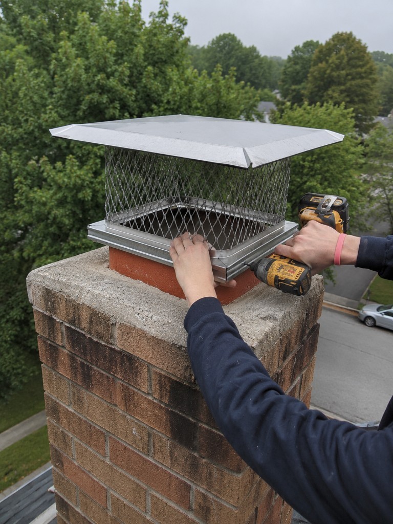 Technician securing a metal chimney cap on a brick flue